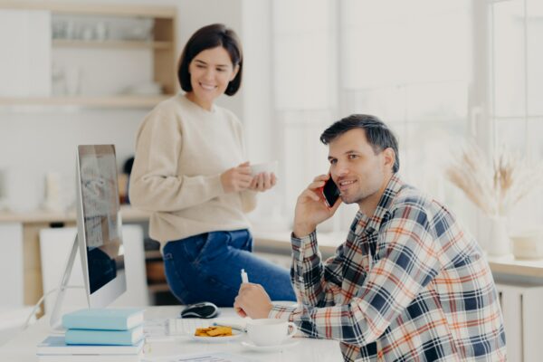 Husband and wife manage finances at home, review bank accounts, pleased man holds mobile phone